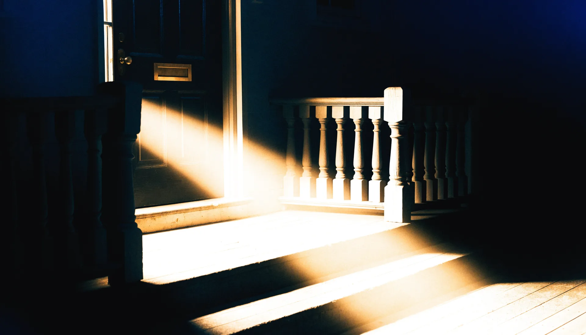 A golden beam of light coming through a dark porch door with a brass mail slot.